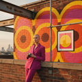 Hackney rooftop at golden hour: the print hanging from scaffolding beside a colour-block mural. Pink Yellow Sun framed and mounted print hanging from scaffolding beside a colour-block mural on a Hackney rooftop at golden hour